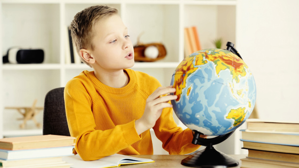 schoolboy in yellow jumper looking at globe near notebook and books on desk  - Fotografie, Obrázek