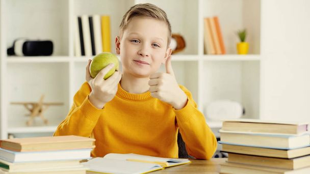 школярка тримає зелене і смачне яблуко, показуючи великий палець вдома
  - Фото, зображення