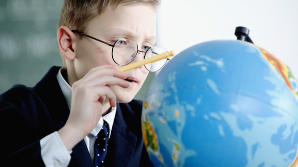 schoolboy in glasses pointing with pencil at globe in classroom  - Fotó, kép
