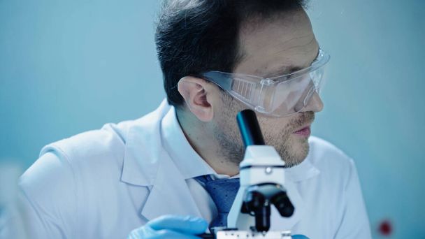 handsome scientist in goggles looking away near microscope in laboratory - Zdjęcie, obraz