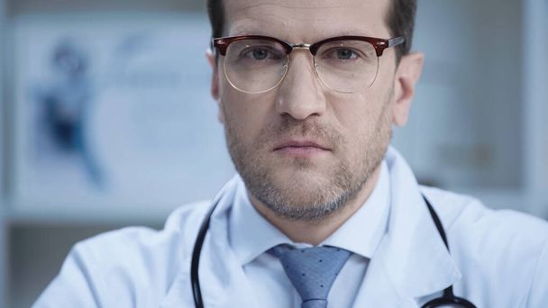 confident doctor in glasses and white coat looking at camera in clinic  - Foto, afbeelding
