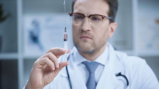 blurred doctor in white coat and glasses holding syringe in clinic  - Foto, imagen