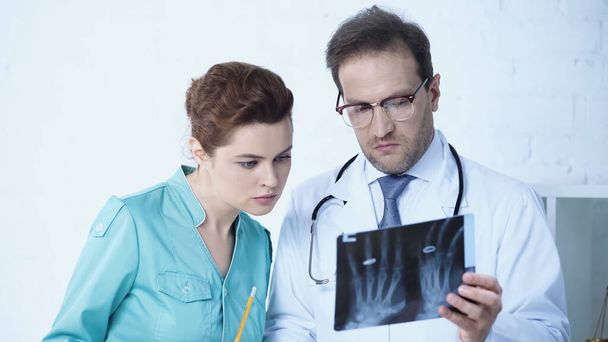 nurse looking at x-ray scan together with serious radiologist in clinic - Foto, afbeelding