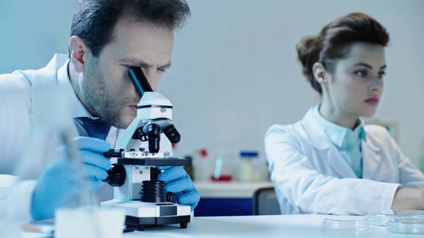 scientist making looking through microscope near pretty colleague sitting in laboratory - Photo, Image
