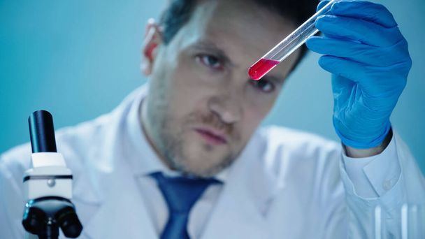 serious scientist looking at test tube with red liquid in clinical laboratory - Фото, изображение