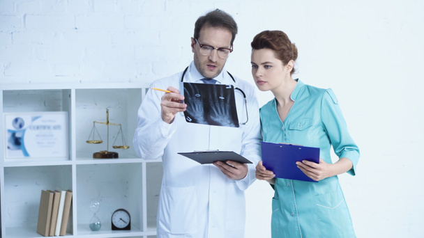 radiologist in glasses and pretty nurse standing with clipboards and looking at x-ray scan - Foto, Bild