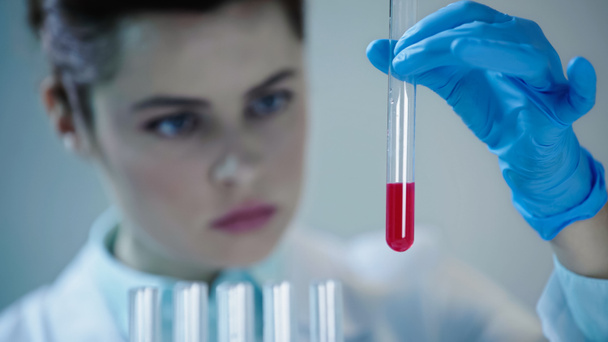 жінка-вчена в латексній рукавичці тримає пробірку з червоною рідиною в лабораторії
 - Фото, зображення