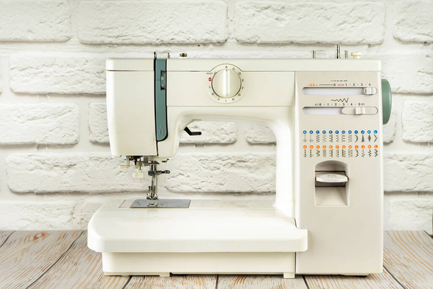 Modern multi operation sewing machine, assortment of different stitches for decorating clothes on table in tailor's workshop or atelier on white brick background. - Foto, Bild