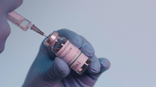 cropped view of scientist in latex gloves filling in syringe with vaccine from bottle with lettering isolated on grey  - Foto, afbeelding
