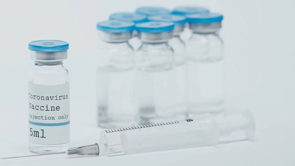 close up of syringe near bottles with coronavirus vaccine and lettering isolated on white - Foto, afbeelding