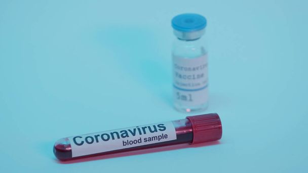 blood sample in test tube with lettering and blurred bottle with coronavirus vaccine on blue - Foto, afbeelding