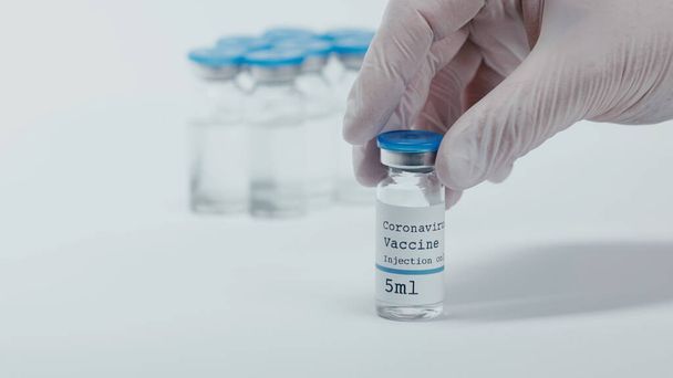 cropped view of person holding bottle with coronavirus vaccine liquid on white  - Foto, afbeelding