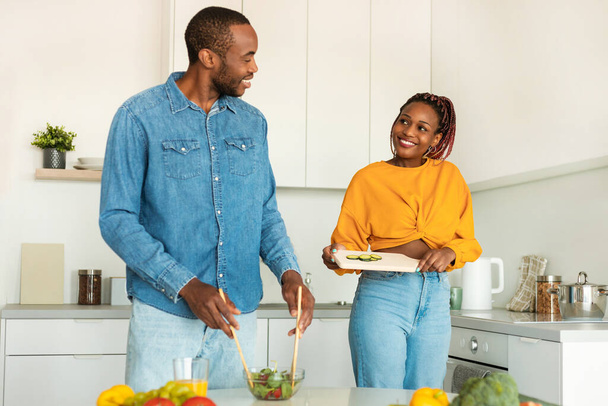 Happy african american spouses cooking fresh vegetable salad together in kitchen, wife and husband enjoying preparing healthy food and spending time at home, copy space - Foto, immagini