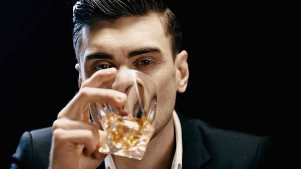 Businessman in formal wear holding glass and drinking whiskey isolated on black  - Foto, Imagem