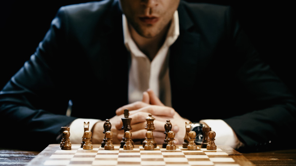 Cropped view of chess on board near blurred businessman in suit isolated on black  - Photo, Image