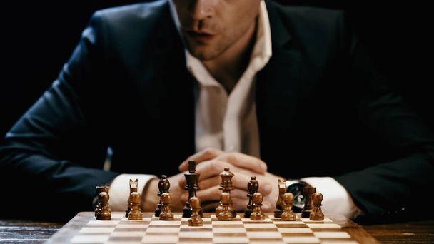 Cropped view of businessman sitting near chess on board isolated on black  - Zdjęcie, obraz