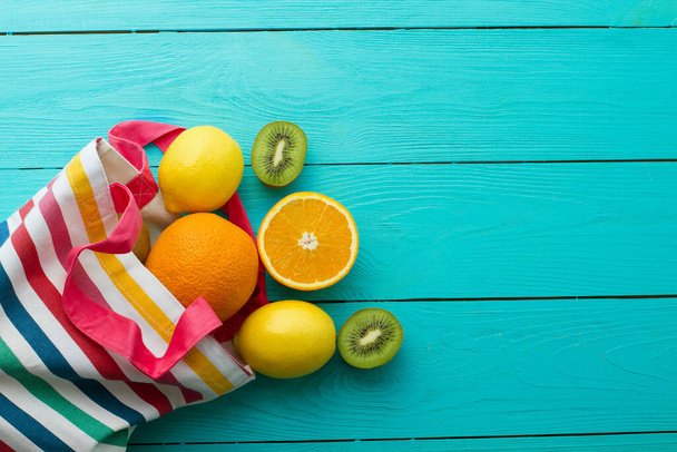 青い木製の背景に夏の楽しい時間と果物。モックアップし、絵。オレンジ、レモン、キウイフルーツをテーブルの上に袋に入れます。トップビューとモックアップ - 写真・画像