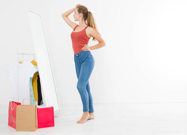 Concetto di vendita. Ragazza bionda in jeans e maglietta. Giovane donna in buona forma del corpo guardando specchio e perdere peso. Copia spazio - Foto, immagini