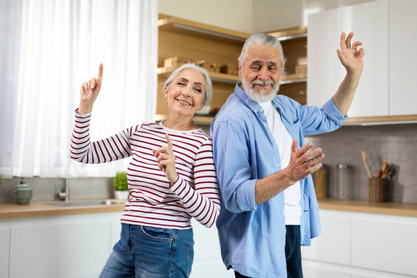 Домашнє задоволення. Радісні старші подружжя танцюють разом у кухонному інтер'єрі, щасливі веселі літні чоловіки та жінка дуріють та сміються, насолоджуючись проводити час один з одним, копіювати простір
 - Фото, зображення