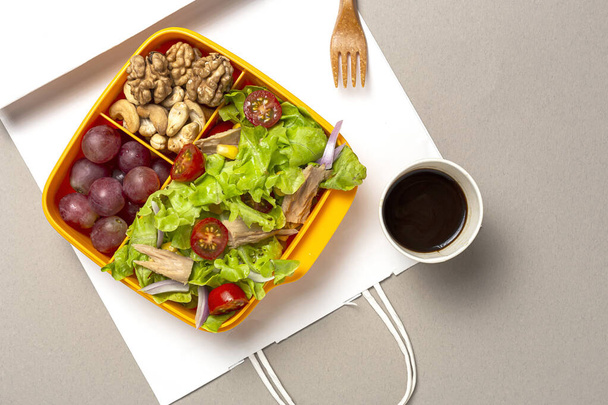 Healthy Food in Plastic container ready to eat with homemade lettuce salad with tomato, onion, corn, tuna, roga grapes, walnuts and cashews in paper bag fro, above. Take away concept - Photo, image
