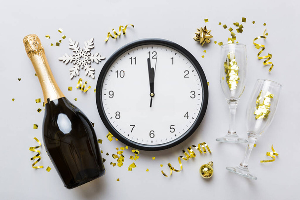New year celebration concept with a bottle of champagne and two glasses toasting. Christmas gift box, alarm clock and fir tree branch on colored table. Top view Copy space. - Photo, image
