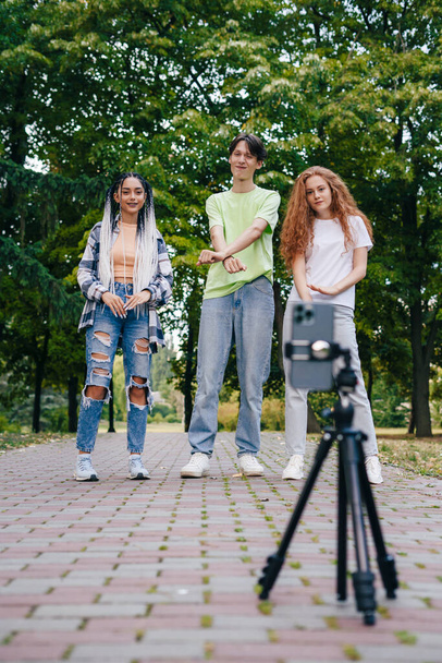 Modern trendy young people dancing in the summer in the park, recording a video with mobile phone. Gen Z group of friends using gadget and having fun outdoors. - Foto, imagen