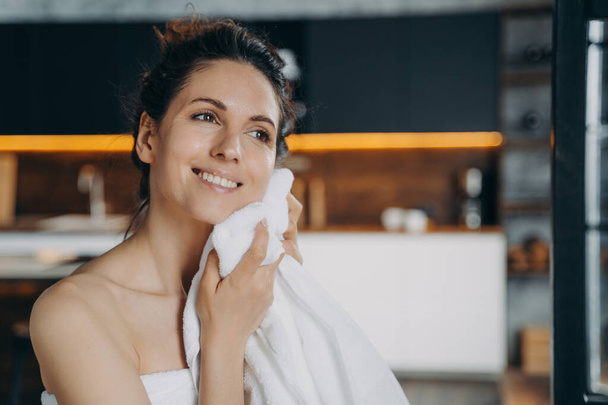 Happy young latina girl wiping face with cotton towel after morning washing, enjoying delicate touch. Smiling female drying her glowing healthy skin after shower. Skincare treatment, self-care concept - Foto, afbeelding