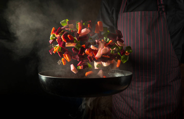 Chef prepares food in a hot pan with steam on a black background. The concept of restaurant and hotel service. Grande cuisine - Zdjęcie, obraz