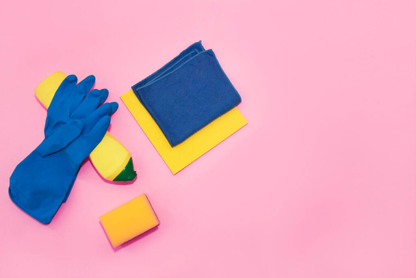 household supplies for cleaning the apartment, a blue rag, gloves and a yellow sponge on a pink background - Foto, Bild