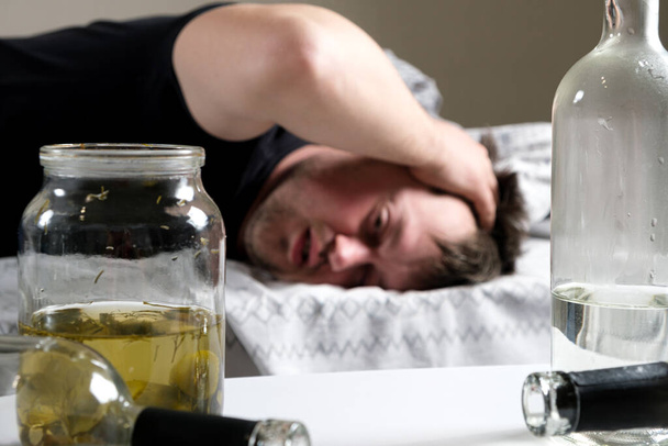 Ein Betrunkener liegt im Bett und hält sich die Hände an den Kopf. Kater, alkoholisches Delirium - Foto, Bild