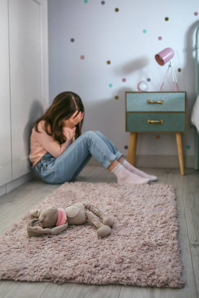 Unrecognizable sad girl with anxiety sitting on the floor of her bedroom with stuffed animal toy lying. Selective focus on stuffed animal in foreground - Fotografie, Obrázek