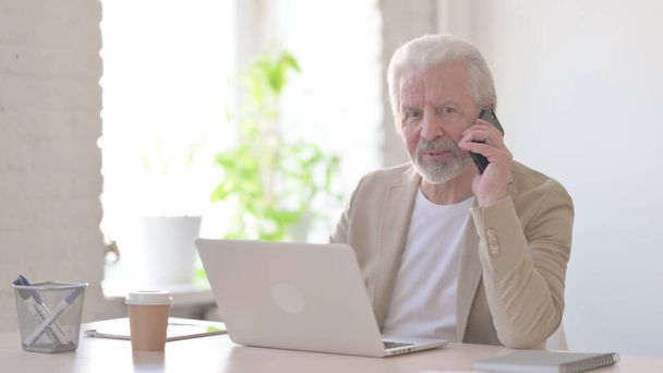 Senior Old Man Talking on Phone while using Laptop in Office - Zdjęcie, obraz