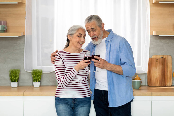 Portrait Of Romantic Elderly Couple Drinking Wine And Relaxing Together In Kitchen, Happy Senior Man And Woman Clinking Glasses And Smiling, Loving Spouses Enjoying Date At Home, Copy Space - Foto, Imagem