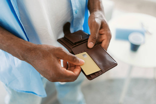 Unrecognizable black guy taking out credit card from his wallet, standing at home, closeup, copy space. Modern payments and online banking concept - Valokuva, kuva