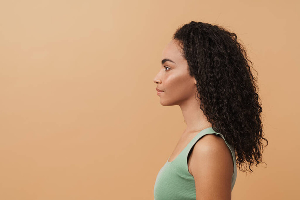 Young black woman with wavy hair posing and looking aside isolated over beige background - Foto, immagini