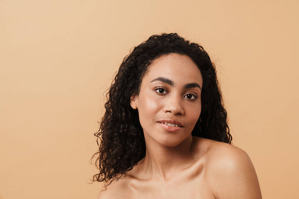 Shirtless black woman with wavy hair posing and looking at camera isolated over beige background - Photo, image