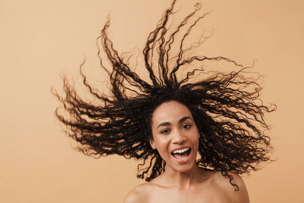 Shirtless black woman laughing while making fun with her hair isolated over beige background - Foto, imagen