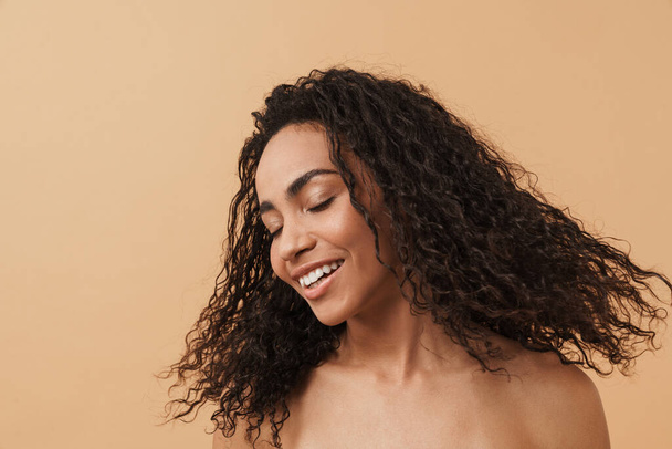 Shirtless black woman with wavy hair laughing at camera isolated over beige background - Fotó, kép