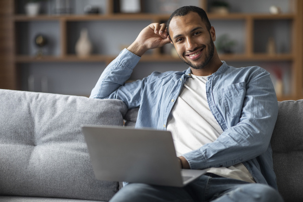 Portrait Of Handsome African American Male Using Laptop While Sitting On Couch At Home, Black Millennial Man Working Remotely On Computer In Living Room And Smiling At Camera, Copy Space - Foto, immagini