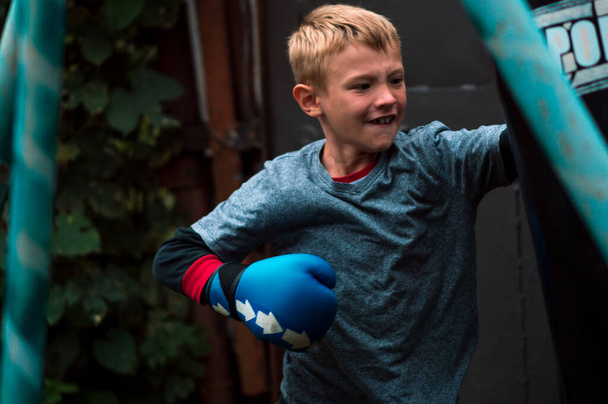 a boy punches a punching bag in blue gloves in the yard - Photo, image
