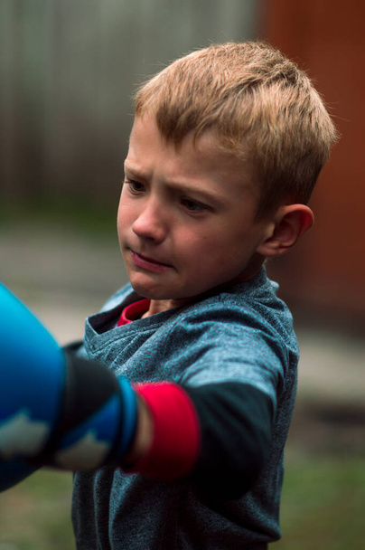 a boy punches a punching bag in blue gloves in the yard - Foto, Imagen