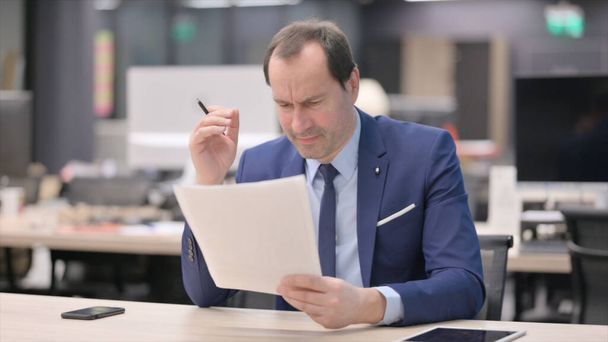 Empresario de mediana edad molesto mientras lee documentos en la oficina - Foto, Imagen