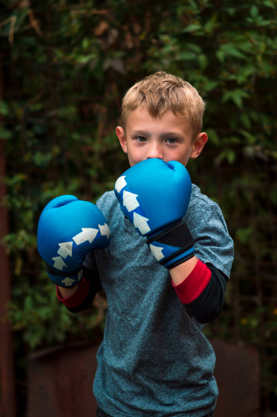 хлопчик в блакитних рукавичках боксерський і міняє руки у дворі
 - Фото, зображення