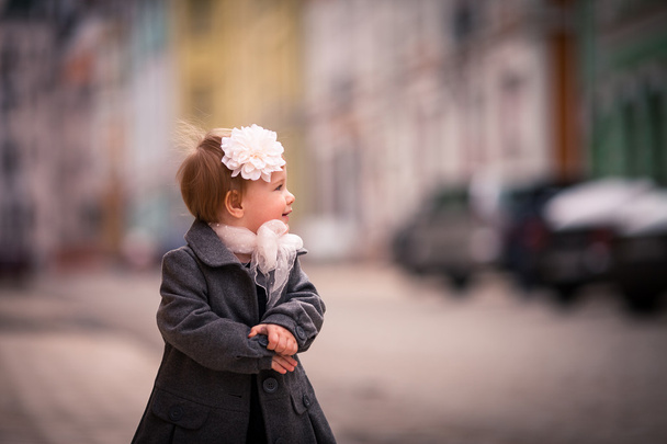 Portrét holčičku v šedém plášti na ulici ve starém městě s legrační úsměv - Fotografie, Obrázek