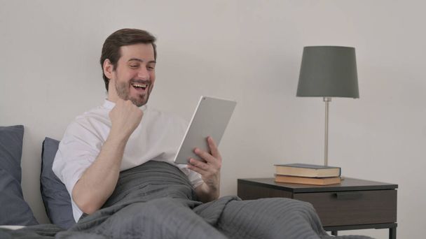 Борода молода людина святкує успіх на планшеті в ліжку
 - Фото, зображення