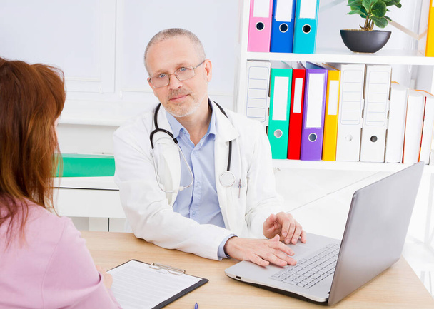 Doctor is talking with woman patient and sitting in medical office.Man in white uniform. Medical insurance. Copy space. Quality medicine concept. - Photo, Image