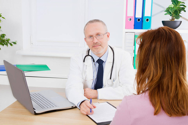 Doctor is talking with woman patient and sitting in medical office.Man in white uniform. Medical insurance. Copy space. Quality medicine concept. - Photo, image