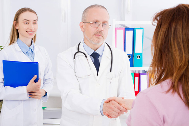doctor posing in office with medical staff, he is wearing a stethoscope. Quality medicine concept. Man in white uniform. Medical insurance. Selective focus. Copy space - Photo, image