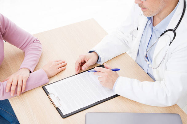 patiënt luistert aandachtig naar een mannelijke arts uitleggen van de symptomen van de patiënt of een vraag zoals ze papierwerk samen te in een overleg bespreken - Foto, afbeelding