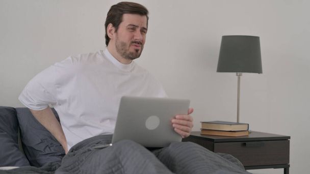 Beard Young Man with Back Pain працює над Laptop in Bed - Фото, зображення
